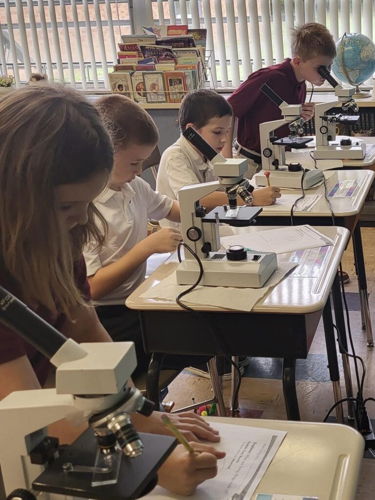 Kennedy Catholic elementary students using microscopes and taking notes during science class.