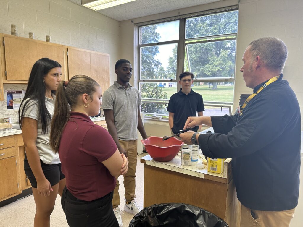Kennedy Catholic teacher leading a hands-on cooking lesson with high school students.