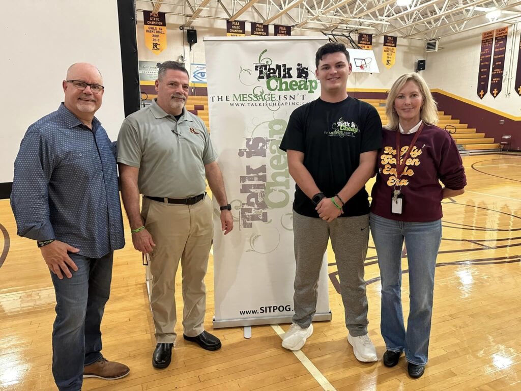 Kennedy Catholic staff and student standing with guest speakers during Talk Is Cheap anti-vaping program in the gymnasium.
