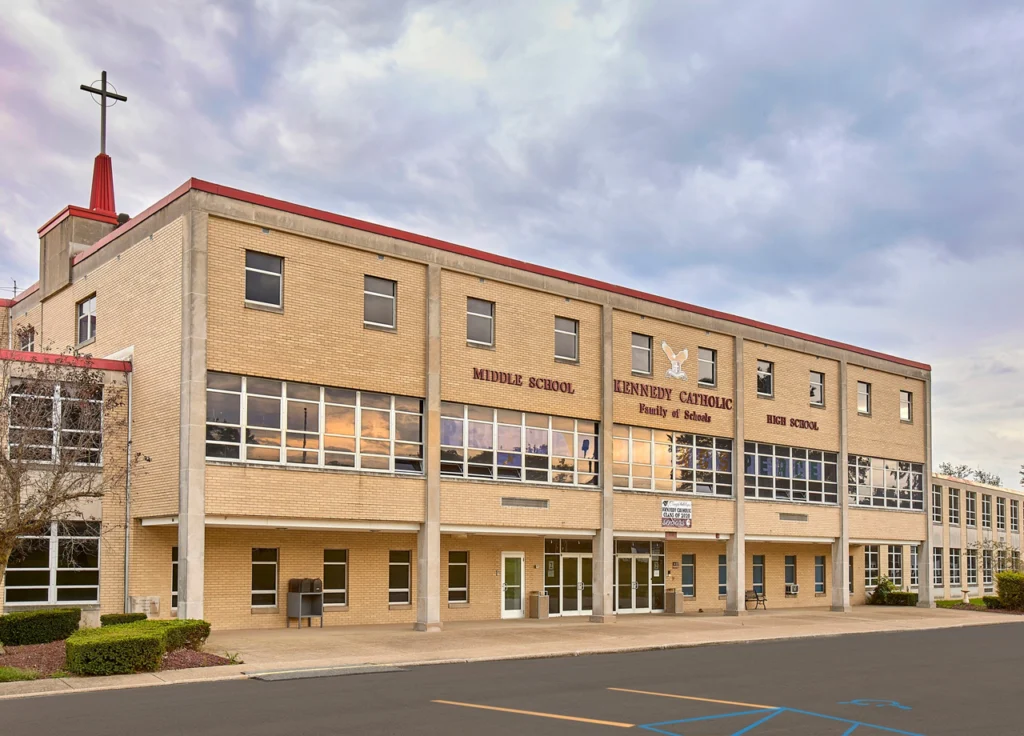 Exterior view of Kennedy Catholic Middle and High School building with cross on rooftop and large windows reflecting the sunset.