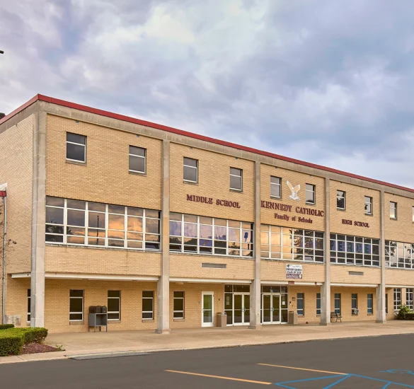 Exterior view of Kennedy Catholic Middle and High School building with cross on rooftop and large windows reflecting the sunset.